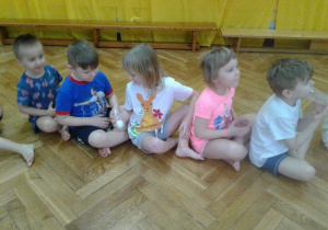 Dzieci siedzą w rzędzie i podają sobie piłeczkę ping-pongową